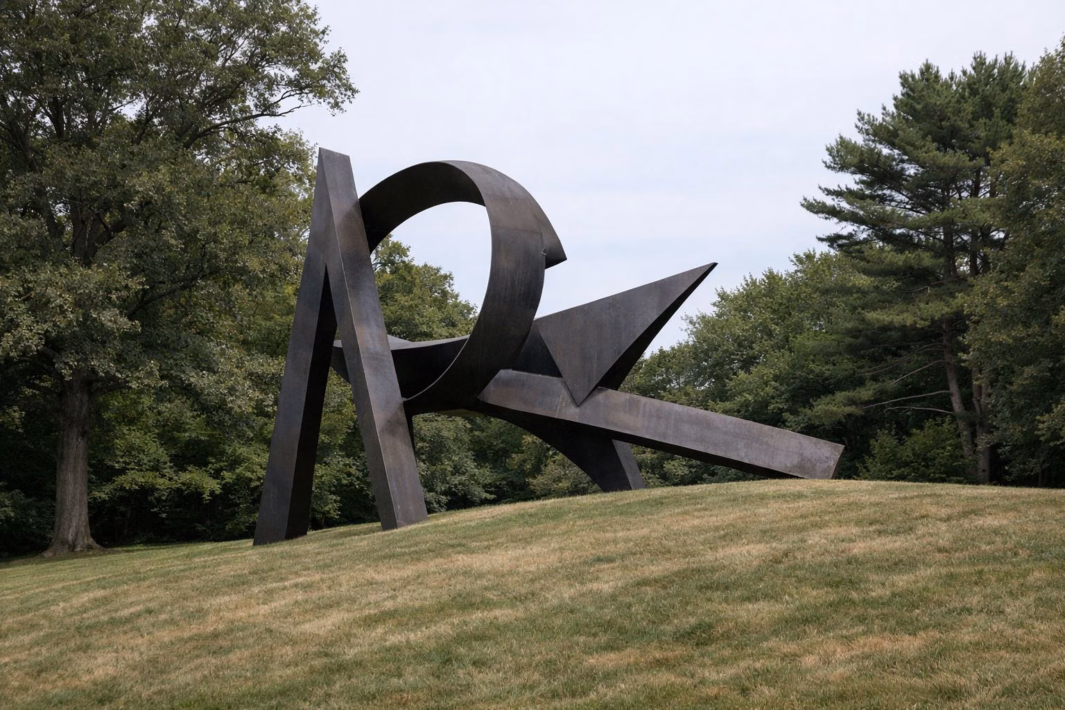 A large abstract steel sculpture on a sloping lawn among mature trees