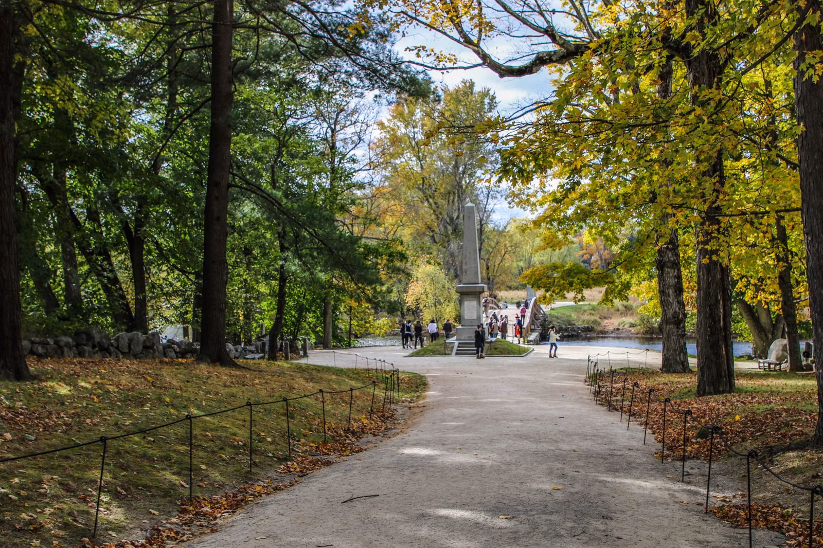 A tree-lined path in fall color leading to the monument by the North Bridge at Minute Man National Historical Park
