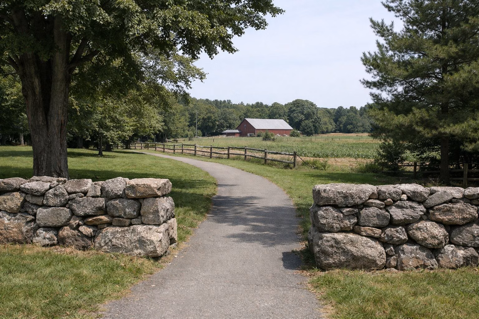 A paved path entering a farm through a gap in an old fieldstone wall, lawn and shade trees